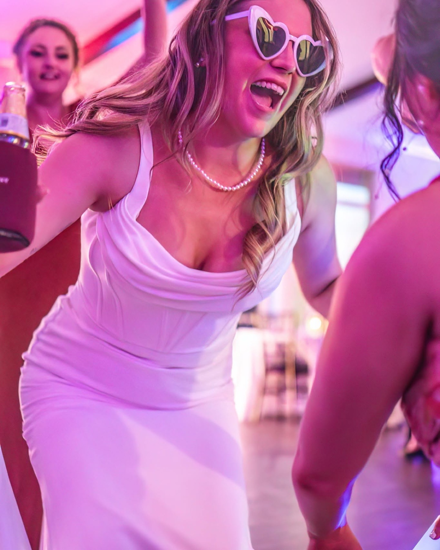 A bride laughs on the dance floor in heart-shaped sunglasses