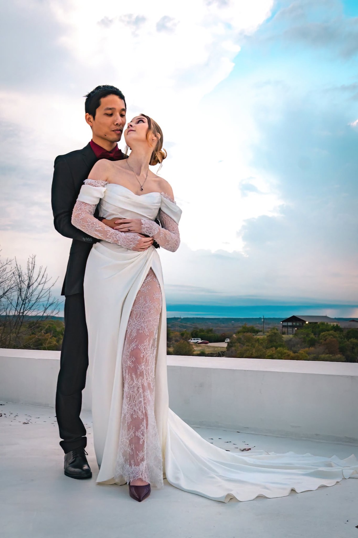 Newlyweds pose together beneath a wide rooftop sky
